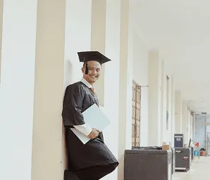 Student in graduation attire walking through a bright school hallway